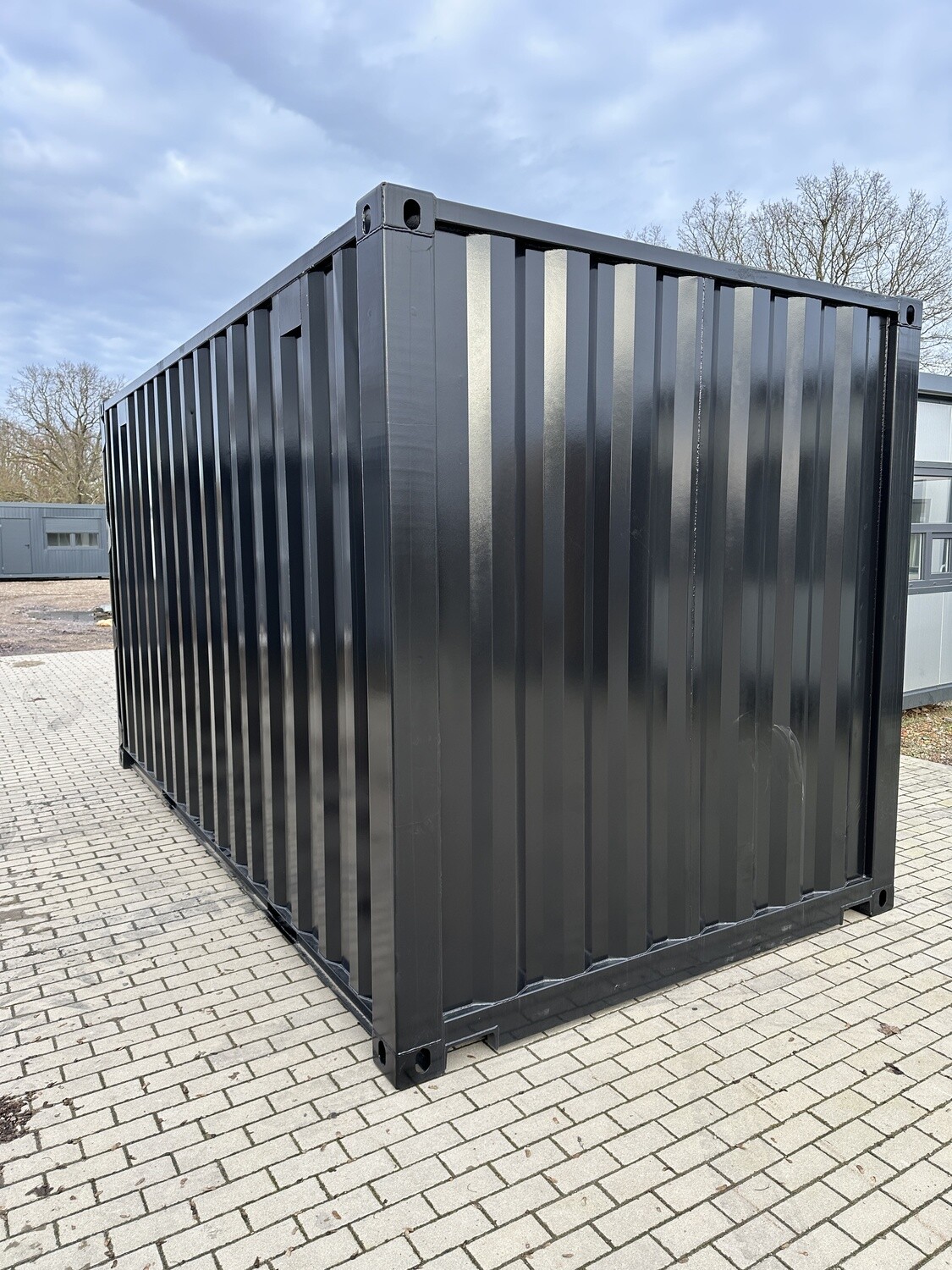 Geschlossene Längs- und Stirnseite des schwarzen Seecontainers, aufgestellt auf einer Pflasterfläche