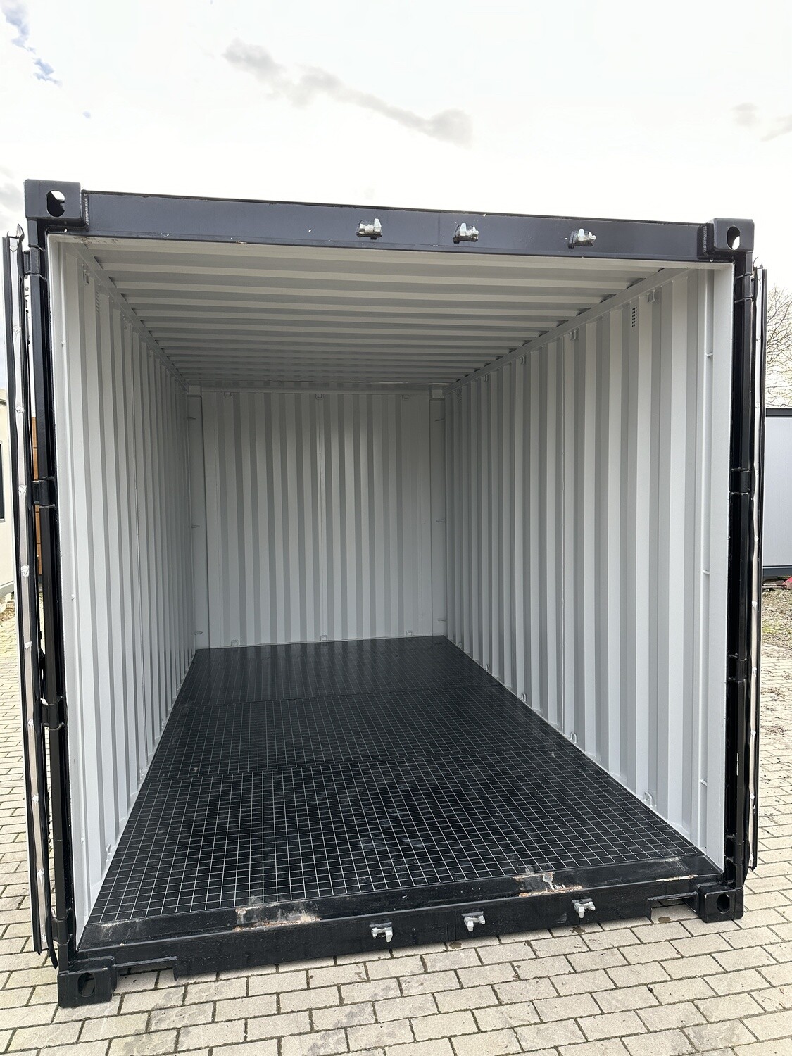 Geöffnete Doppelflügeltür gibt den Blick frei auf helle Innenwände und den dunklen Gitterrostboden