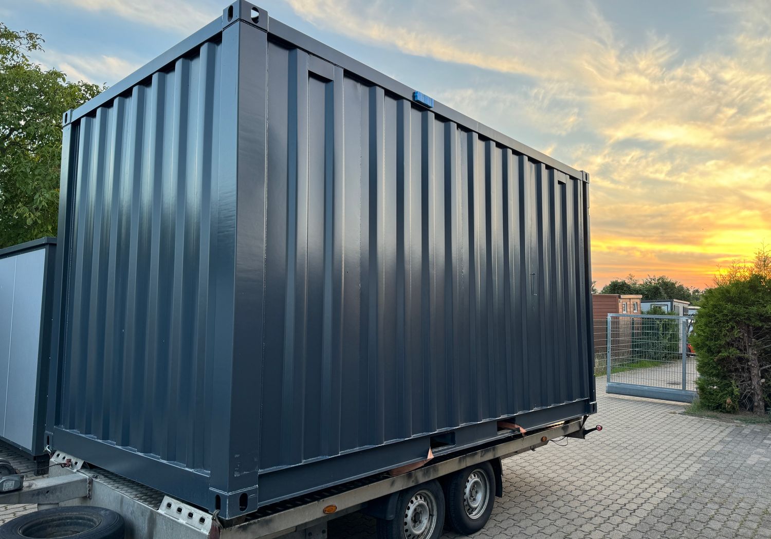 Anthrazitfarbener Lagercontainer auf einem Anhänger, geschlossene Längsseite im Abendlicht