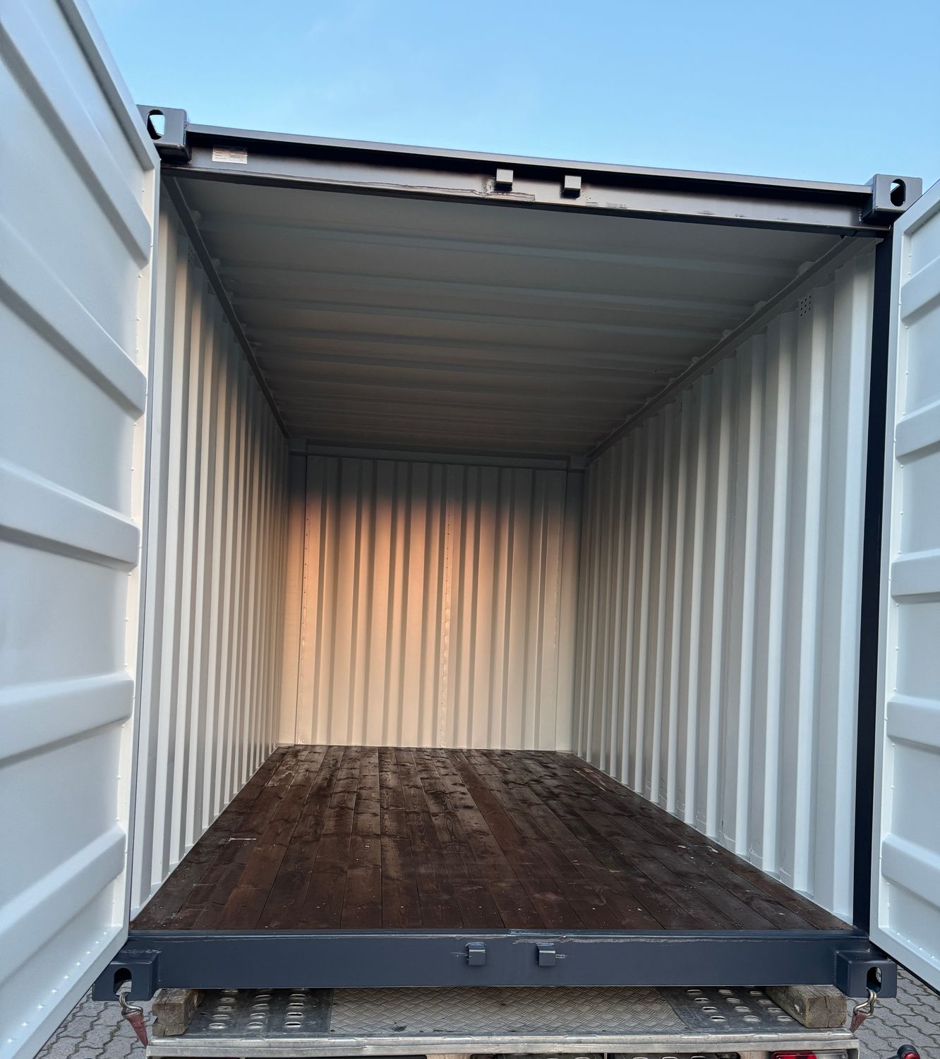 Auf dem Transportfahrzeug geöffneter Seecontainer mit weißen Innenwänden und Holzdielenboden