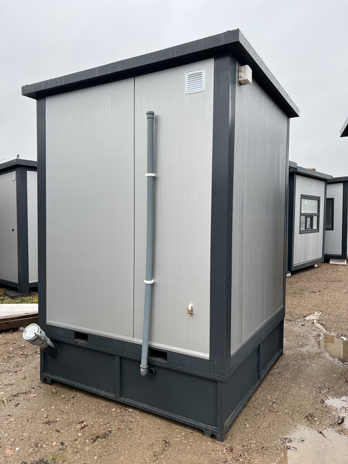 Rückseite des Duschcontainers mit Fallrohr, Lüftungsgitter, Außenzapfhahn und Tankrahmen am Sockel