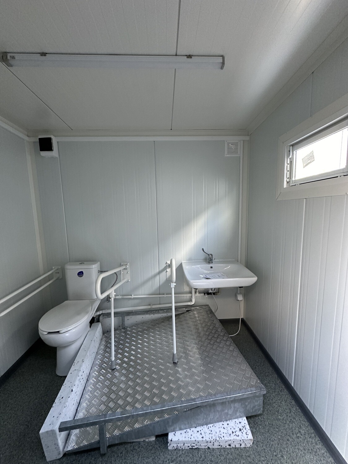 Innenraum mit WC, Stützgriffen und Waschbecken; Riffelblech-Podest und Rampe liegen noch lose im Raum