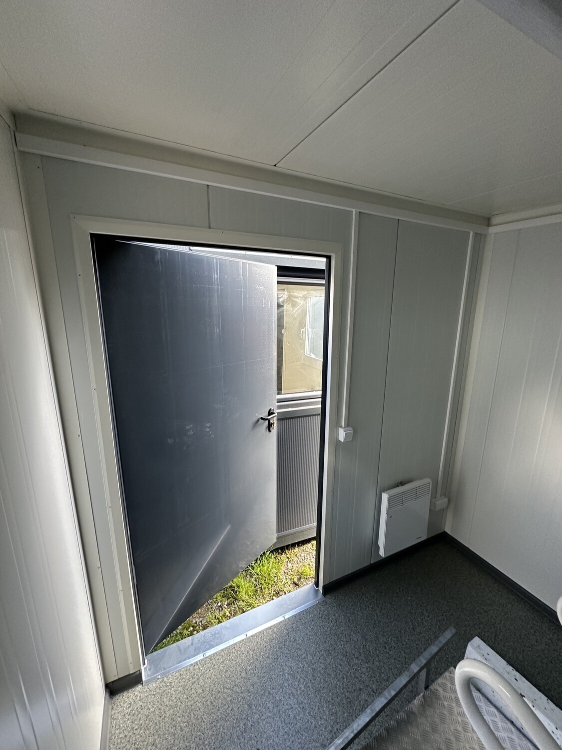 Vom Innenraum aus zur geöffneten Tür fotografiert, mit Wandkonvektor und grauem Bodenbelag