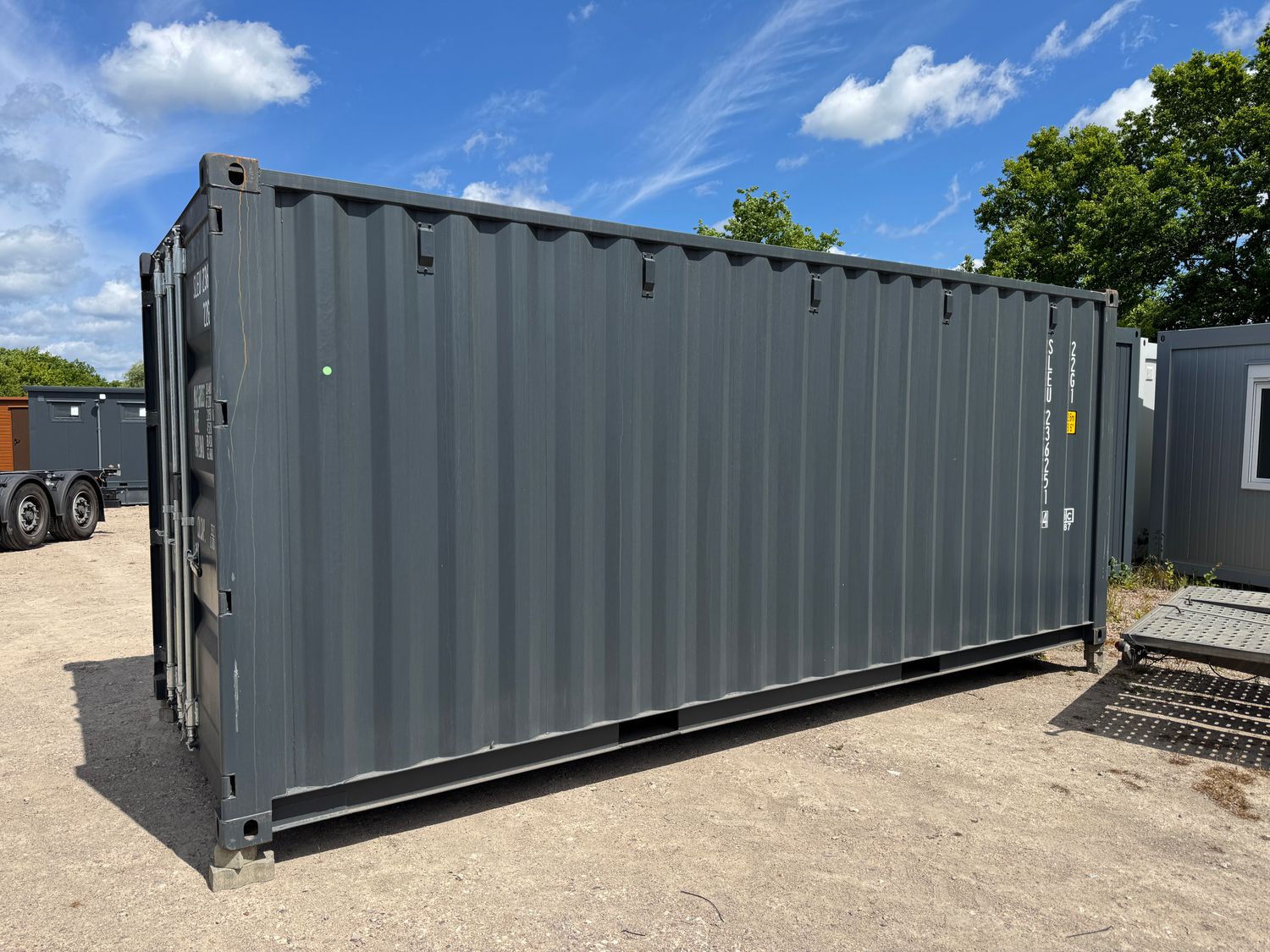 Längsseite des Seecontainers mit gewellter Wand und Staplertaschen, aufgestellt auf einem Schotterplatz