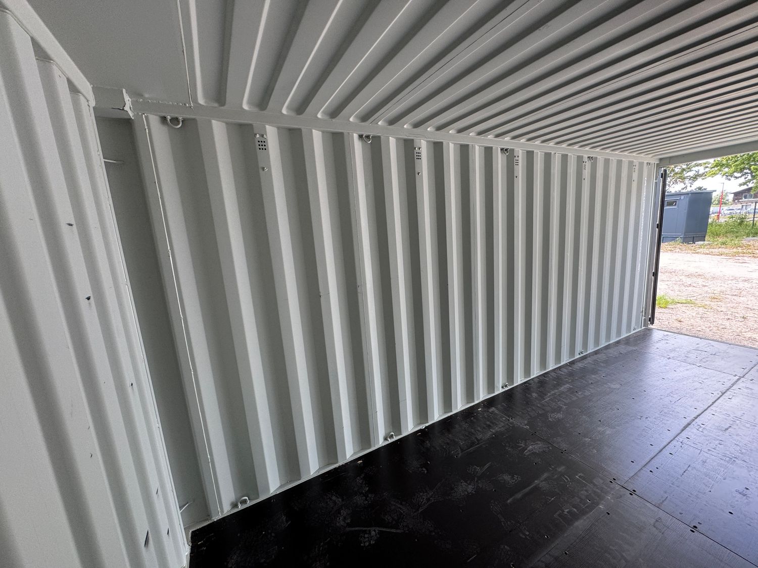 Detailaufnahme im Containerinneren: hell lackierte Wellblechwand mit Zurrösen und dunkler Boden