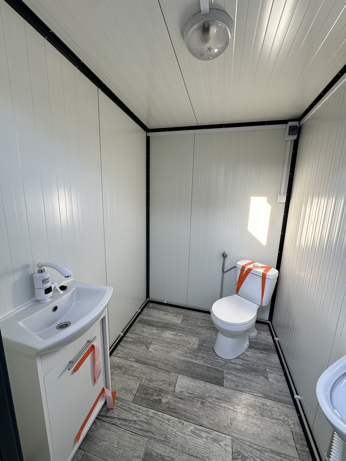 Blick über Waschtisch und Toilette in der hell verkleideten Sanitärkabine des Doppel-WC Containers