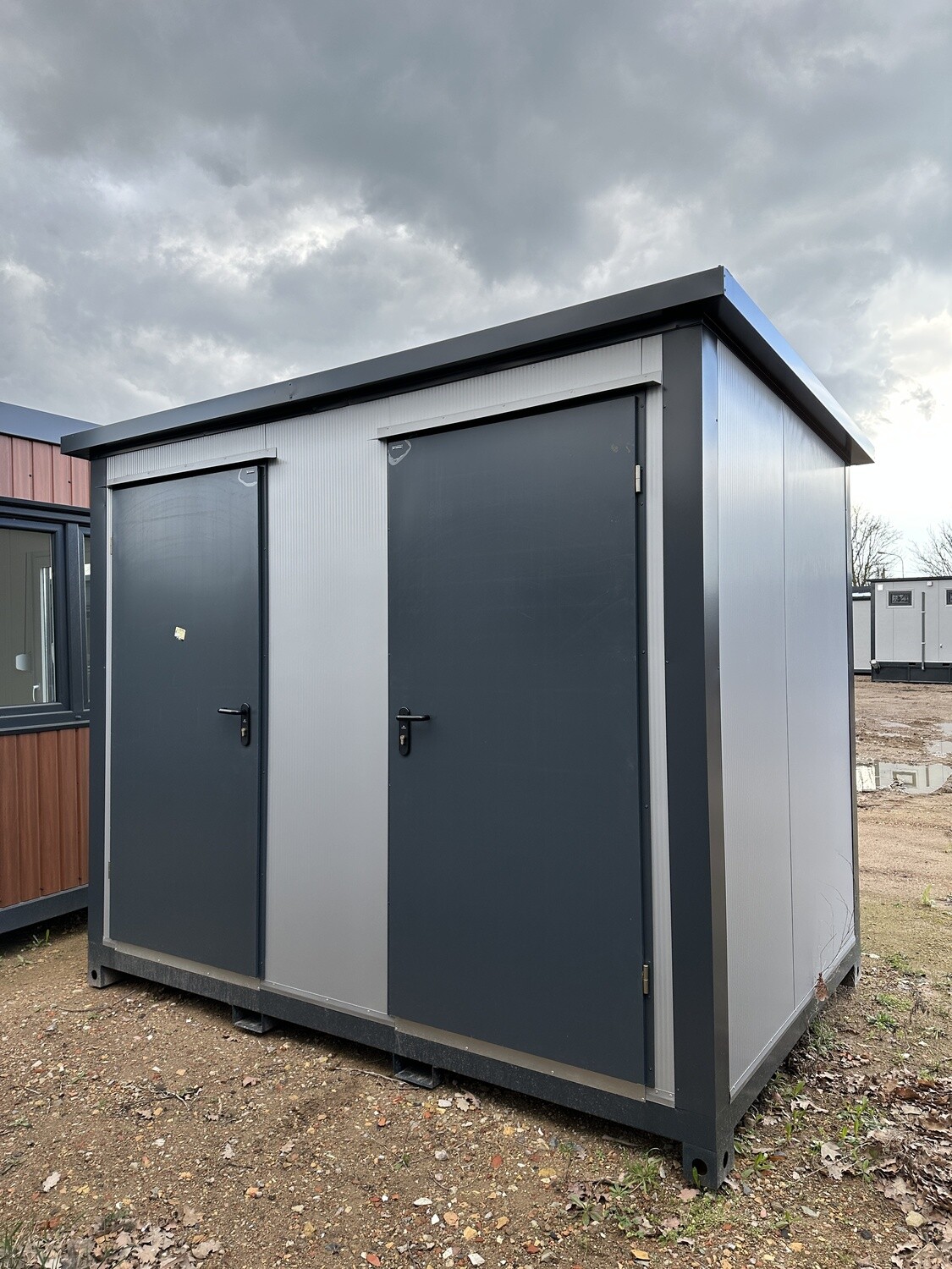 Zwei anthrazitfarbene Türen in heller Wandverkleidung an der Stirnseite des Doppel-WC Containers