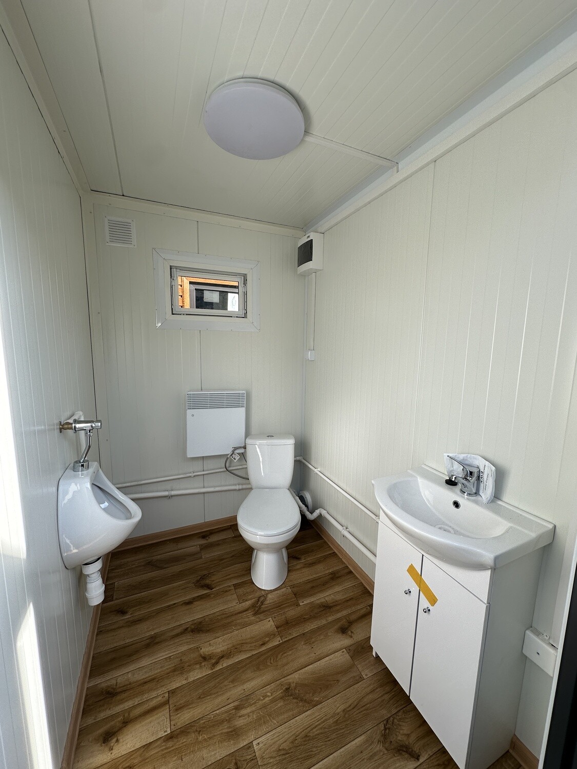 Erste Kabine von innen: Urinal, WC, Waschtisch mit Unterschrank, Konvektor und Holzdekor-Boden