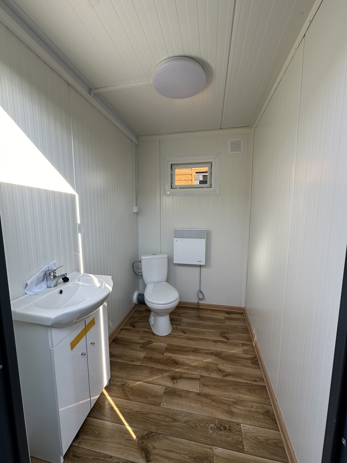 Zweite Kabine mit Waschbecken, Spiegel, WC und Wandkonvektor unter dem kleinen Fenster
