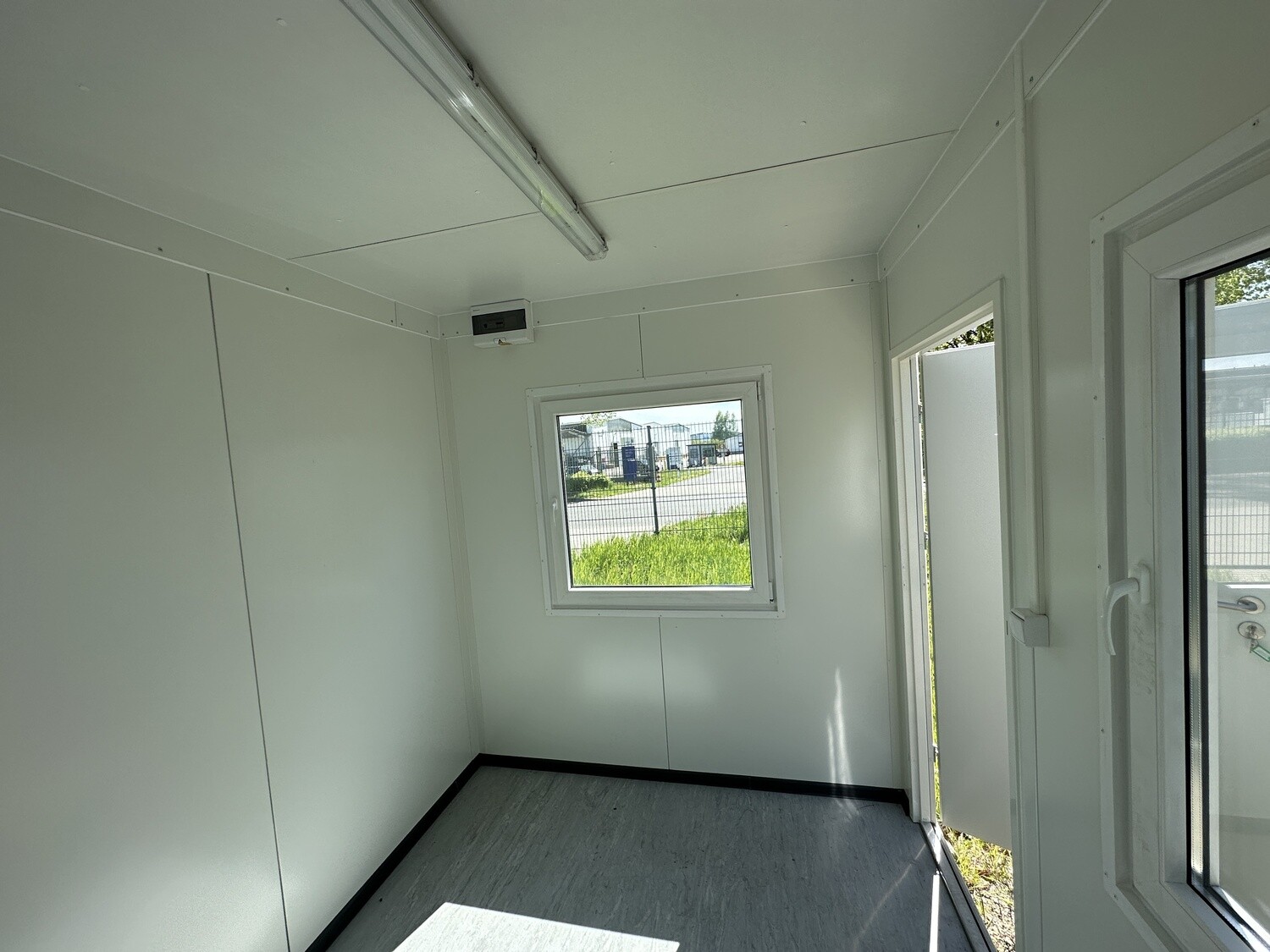 Leerer Büroraum des Pförtnerhauses mit kleinem Fenster, Lichtschalter und Tür mit Glasausschnitt