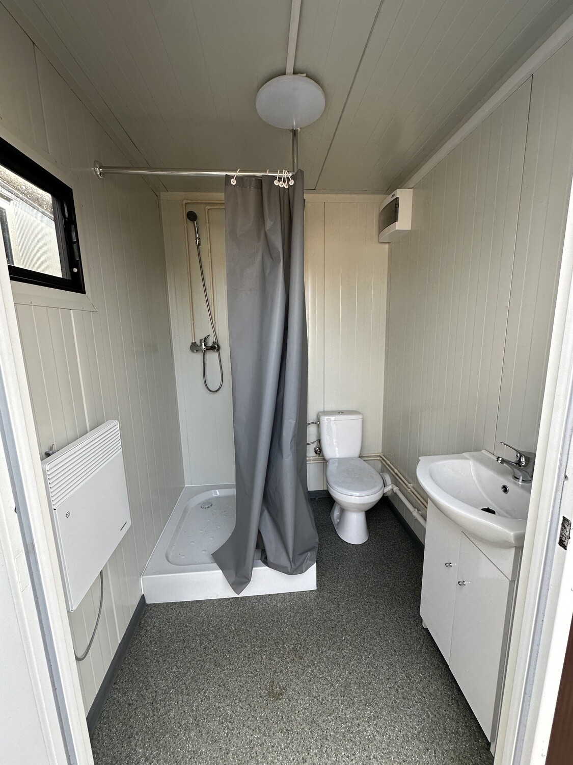 Innenansicht mit Duschtasse samt Vorhang, Toilette, Waschtisch und Wandheizgerät im Duschcontainer