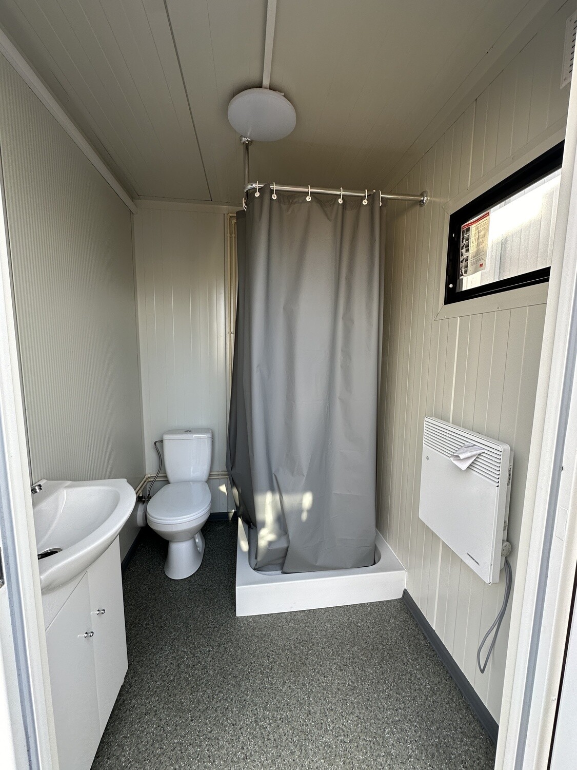 Blick auf Dusche mit zugezogenem Vorhang, Toilette und Waschtisch im Doppel-WC und Duschcontainer