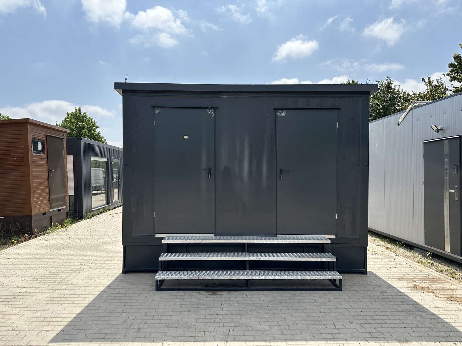 Frontansicht des Sanitärcontainers mit zwei dunklen Eingangstüren über einer dreistufigen Treppe