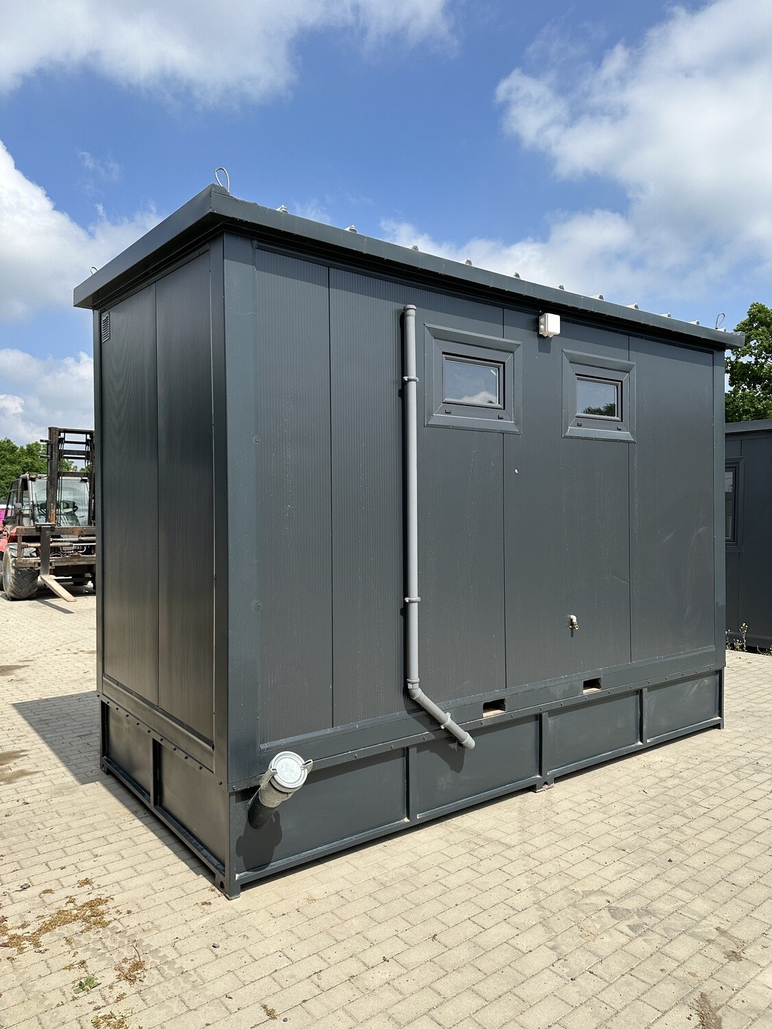 Seitenansicht des Containers mit Fenstern, Regenfallrohr und Anschlussstutzen am Rahmen, auf Pflaster