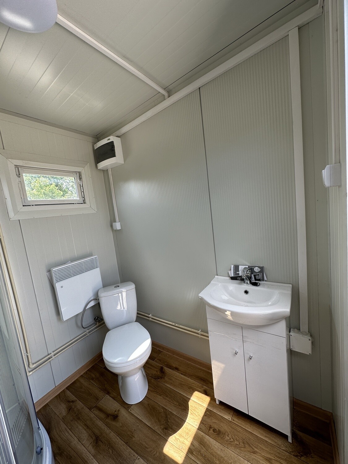 Zweite Sanitärkabine mit WC, Waschtisch samt Unterschrank, Heizgerät und Fenster neben der Trennwand
