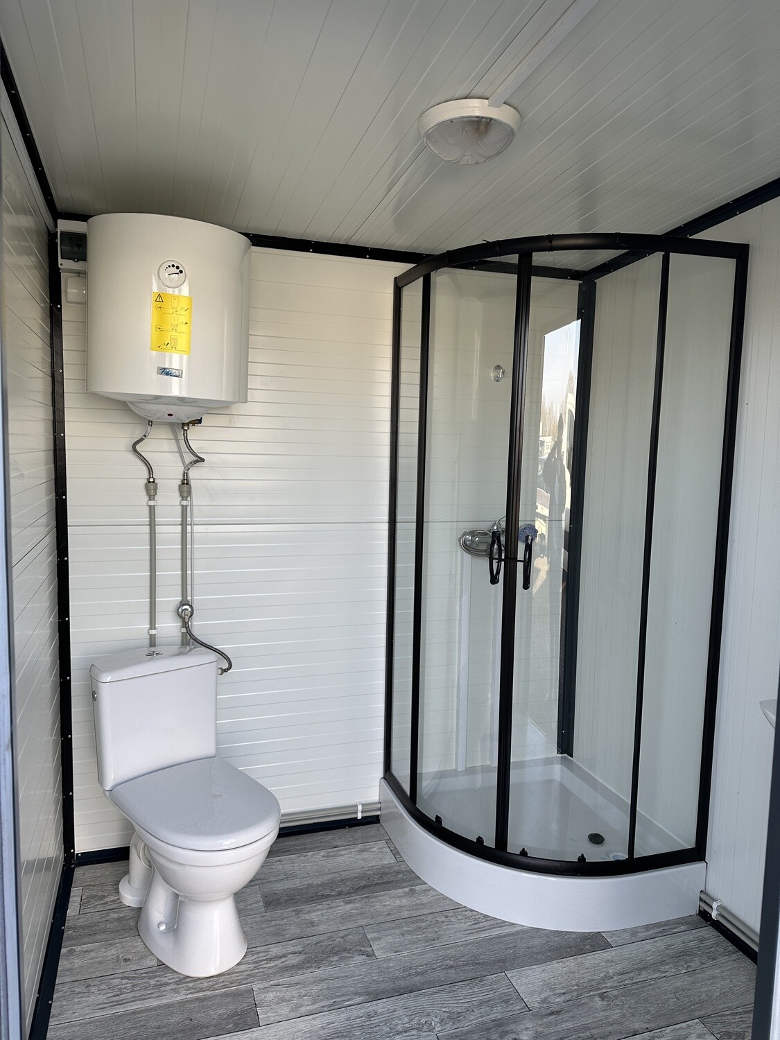 Innenansicht: Warmwasserboiler über dem WC, rechts daneben die Duschkabine mit dunklem Rahmen