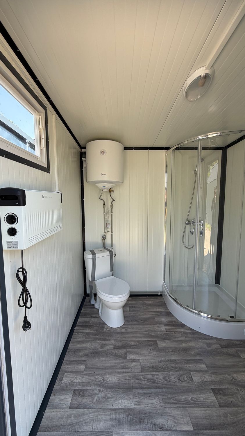 Innenraum mit elektrischem Wandheizgerät, Warmwasserboiler über dem WC und Eckdusche mit Handbrause