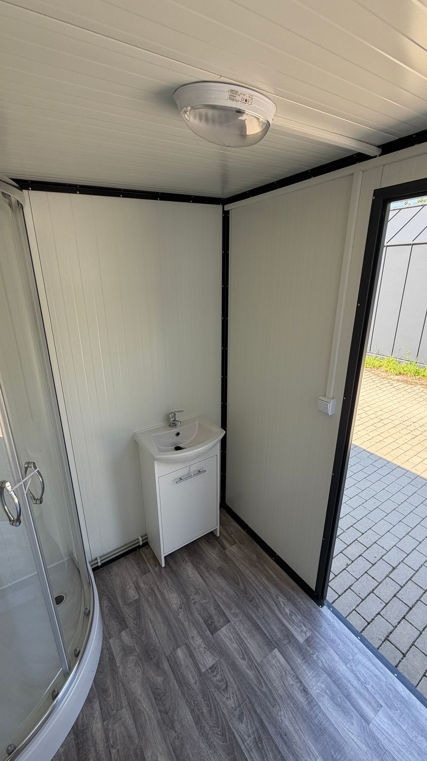 Waschbecken auf Unterschrank neben der Dusche, die geöffnete Tür gibt den Blick auf den Hof frei