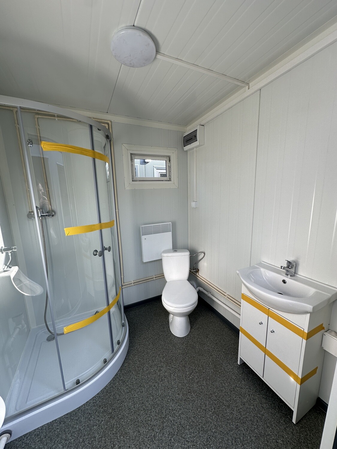 Nasszelle des Doppel-WC-Containers mit Duschkabine, Fenster, Heizgerät, WC und Waschtisch