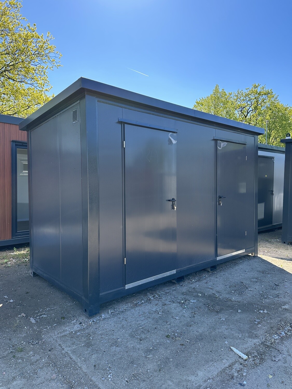 Frontansicht der beiden verschließbaren Türen des dunkelgrauen Sanitärcontainers unter blauem Himmel