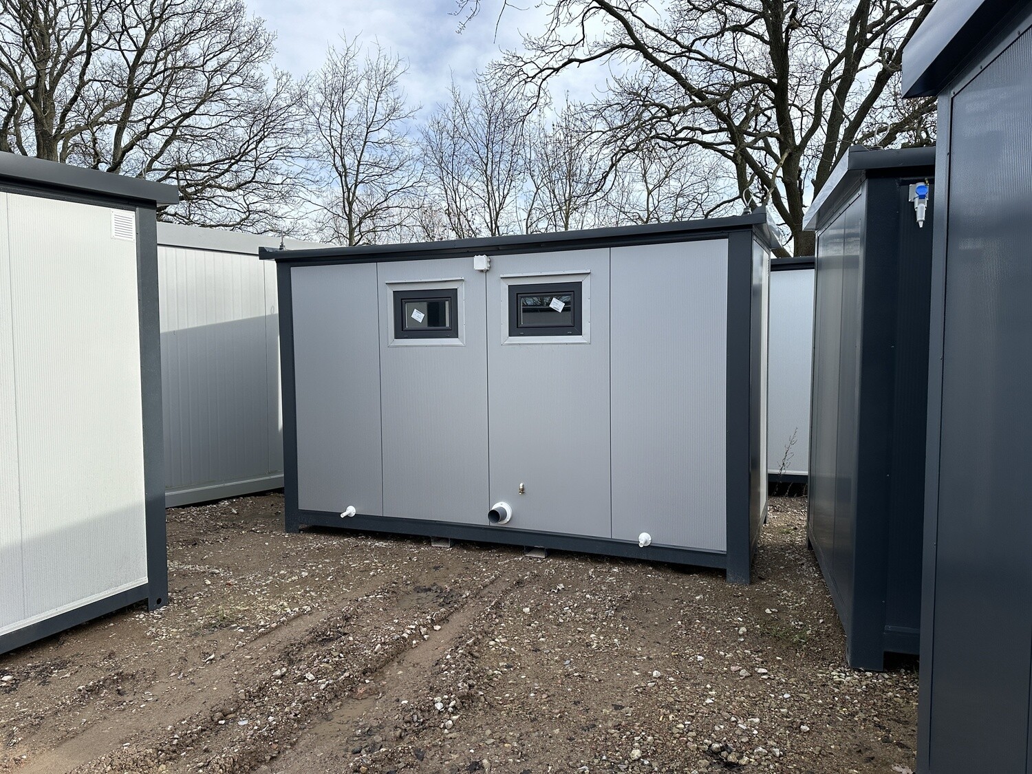 Geschlossene hellgraue Rückwand mit zwei Fenstern und Ablaufstutzen, aufgestellt auf sandigem Untergrund