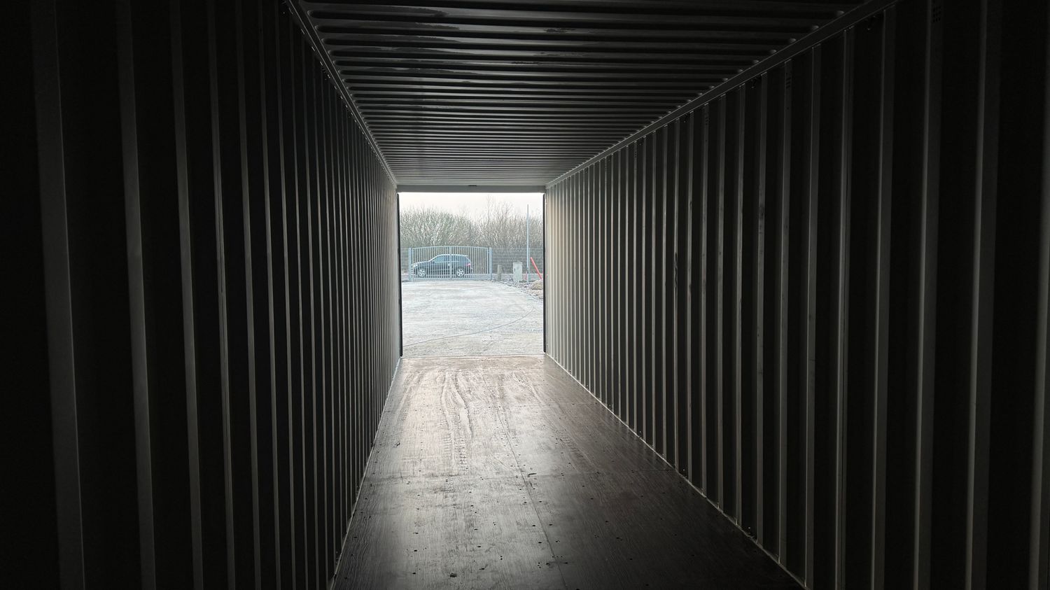 Innenansicht durch den leeren Lagercontainer mit Dielenboden bis zur geöffneten Tür am Ende