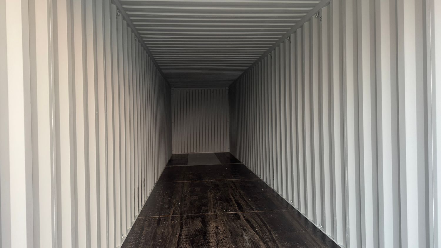 Blick in den geschlossenen Innenraum eines Seecontainers mit hellen Wellwänden und dunklem Boden