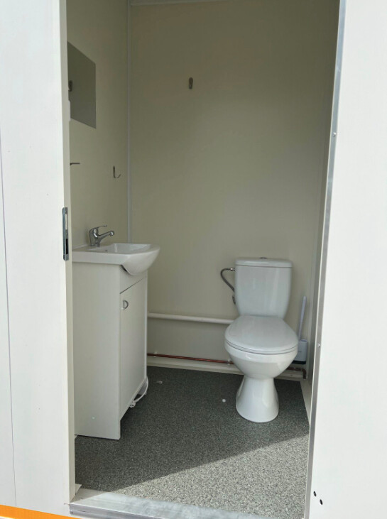 Blick in die WC-Kabine des Büro-Anhängers mit Toilette, Waschbecken auf Unterschrank und hellem Boden