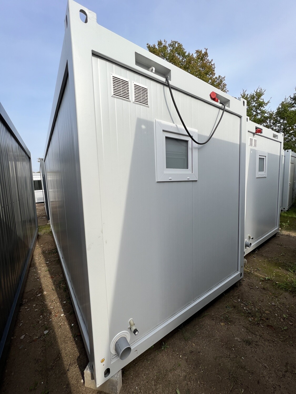 Rückansicht mit Lüftungsgittern, Kippfenster, rotem CEE-Anschluss und Abwasserstutzen am Boden