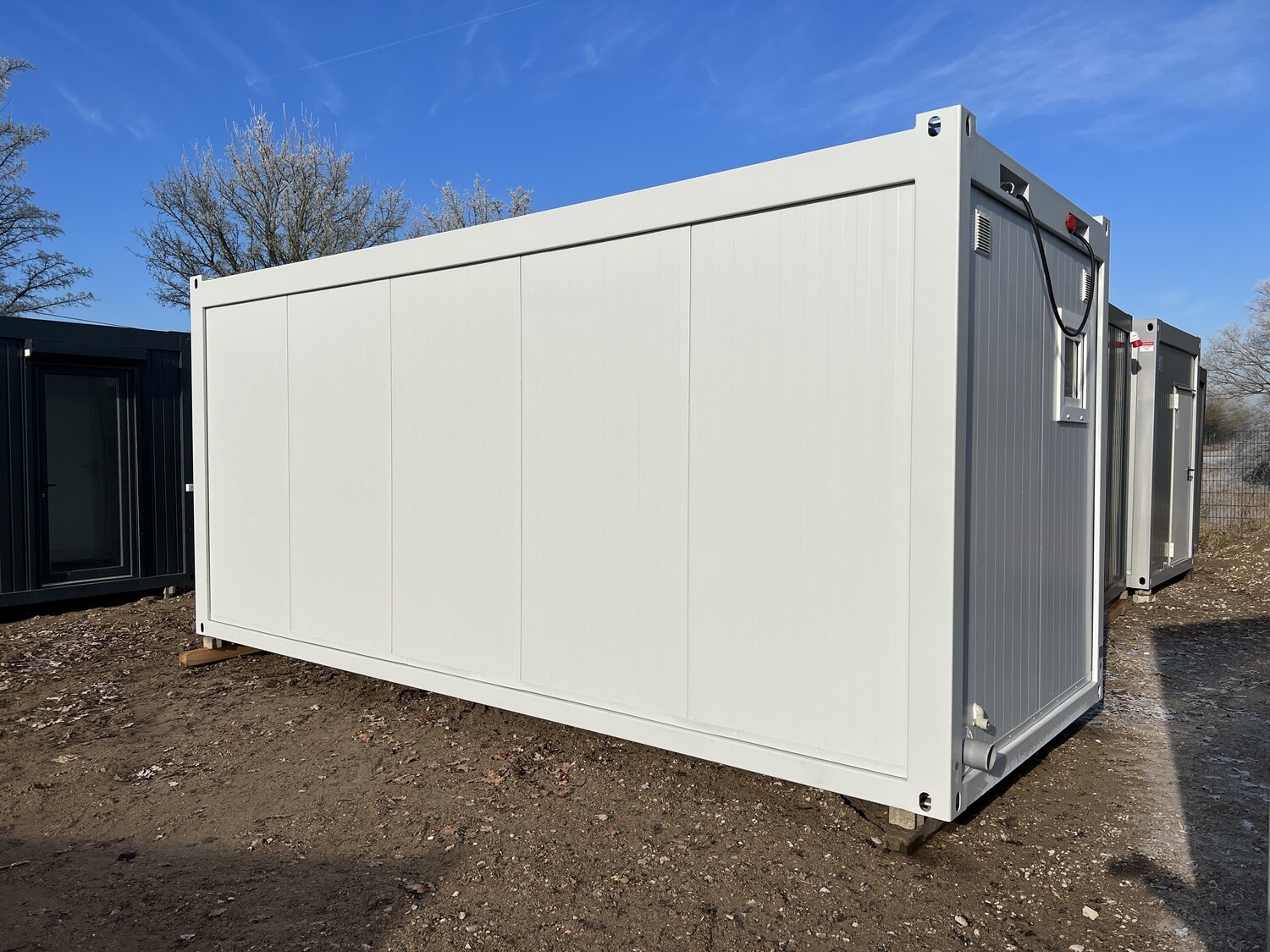 Geschlossene Längsseite des 6,00 x 2,44 m WC-Containers, im Hintergrund weitere Container am Platz