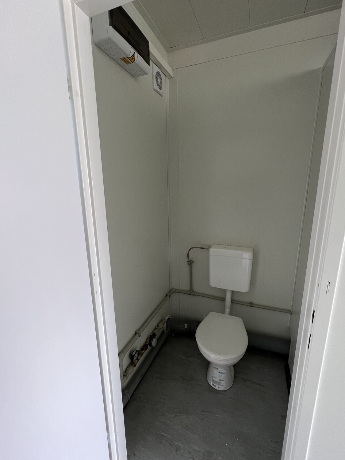 Einzelne Toilettenkabine mit Stand-WC, Spülkasten, Lüftungsgitter und Boiler unter der Decke