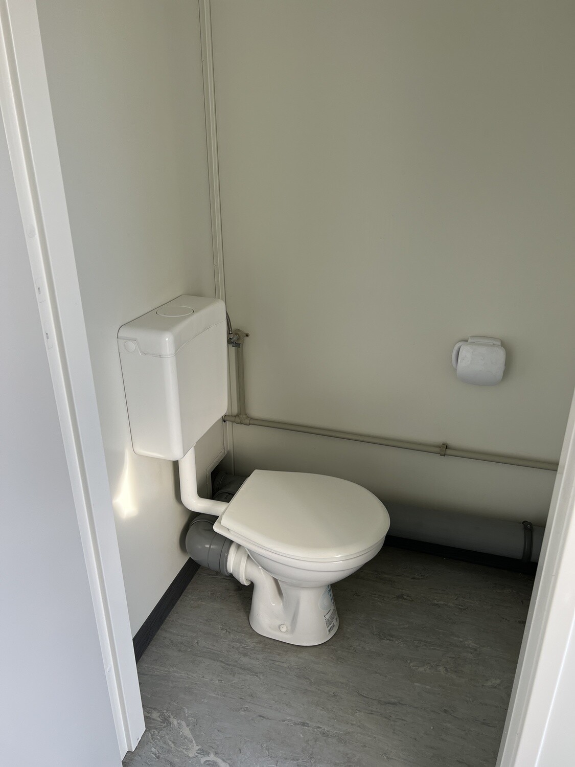 Stand-WC mit wandhängendem Spülkasten, Papierhalter und grauem Bodenbelag in einer Kabine