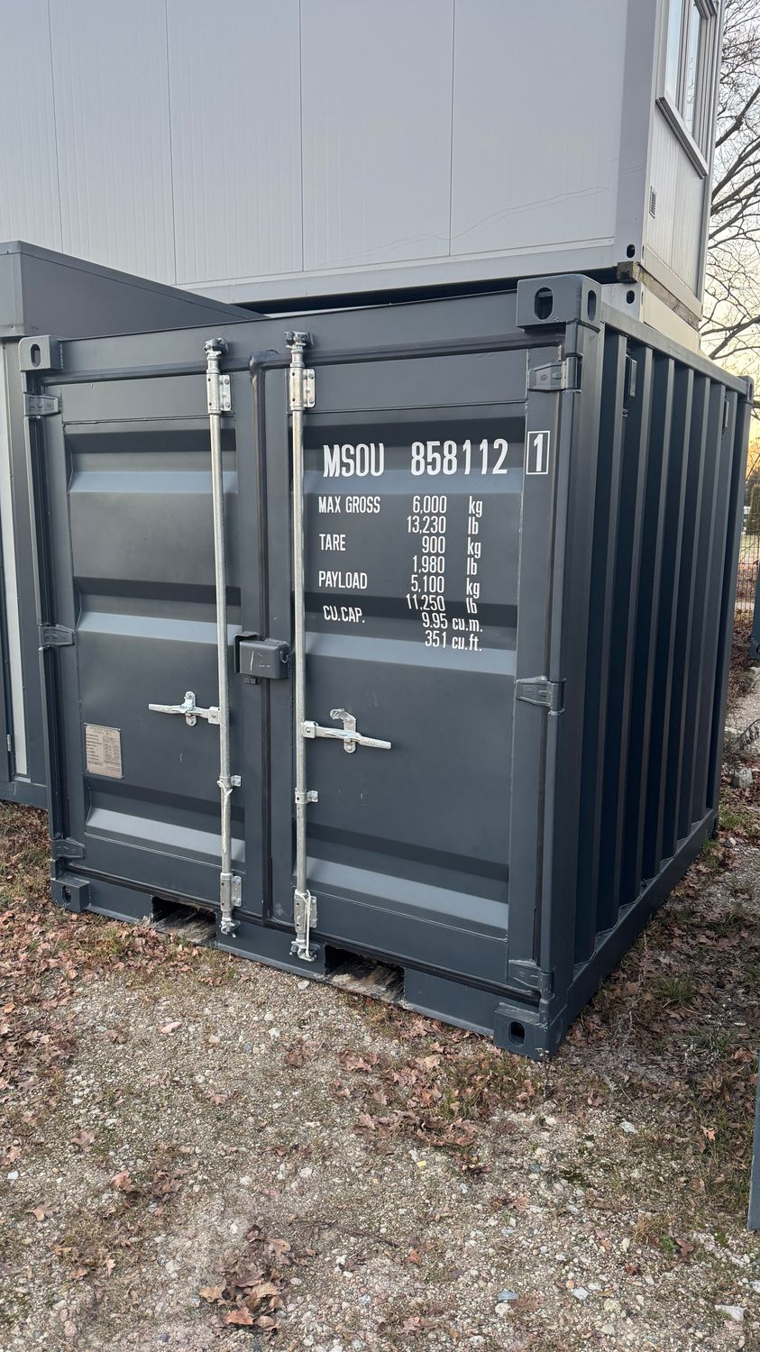 Stirnseite mit Türbeschlägen, Verschlussstangen und aufgedruckten Containerdaten, darüber ein weiterer Container