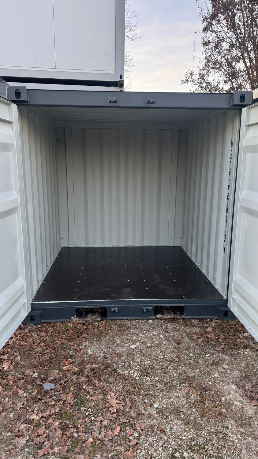 Geöffnete Türen geben den leeren Innenraum des Seecontainers mit Holzboden und gewellten Wänden frei
