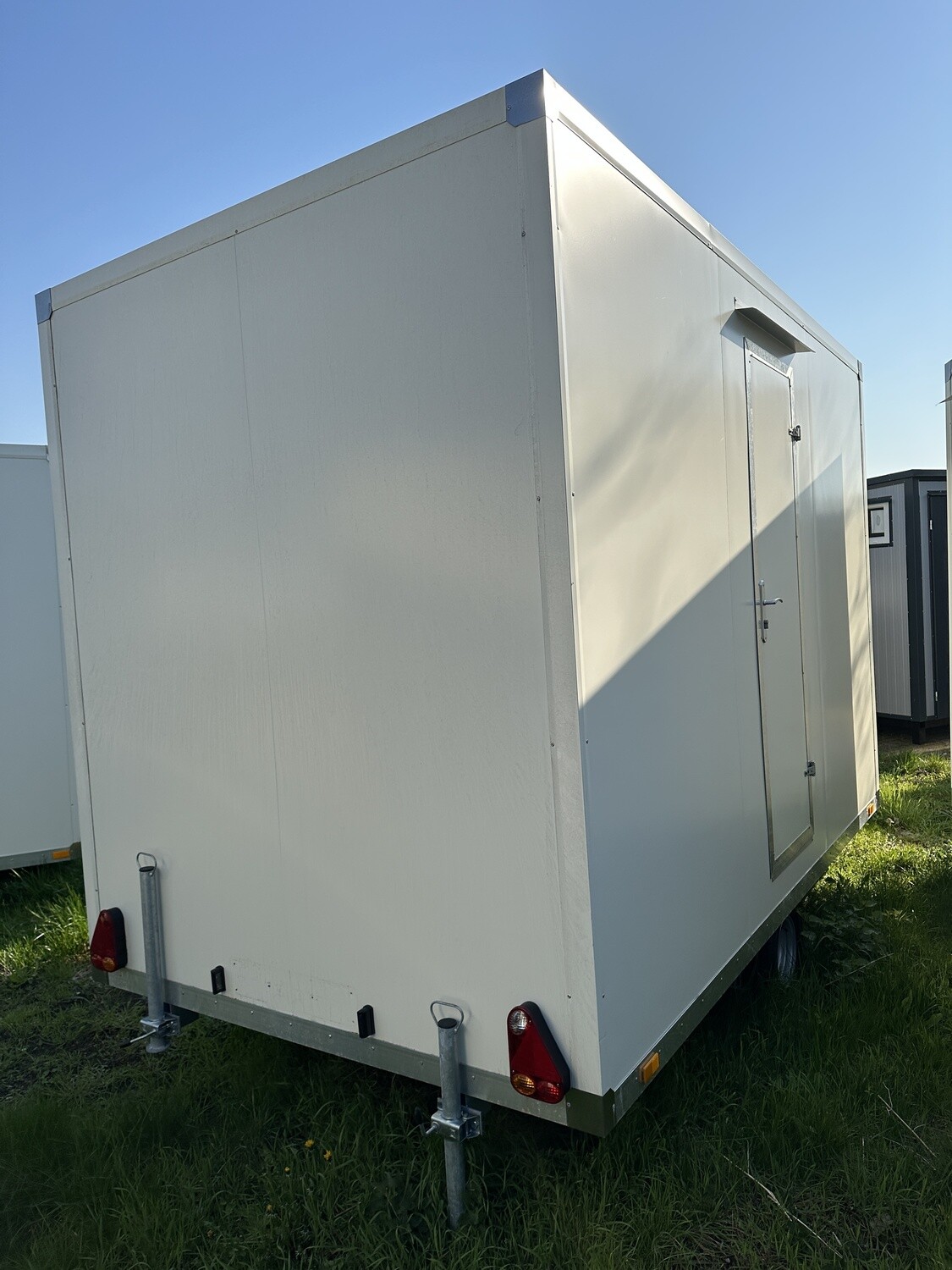 Rückansicht auf der Wiese, mit ausgeklappten Stützfüßen, Rückleuchten und seitlicher Eingangstür