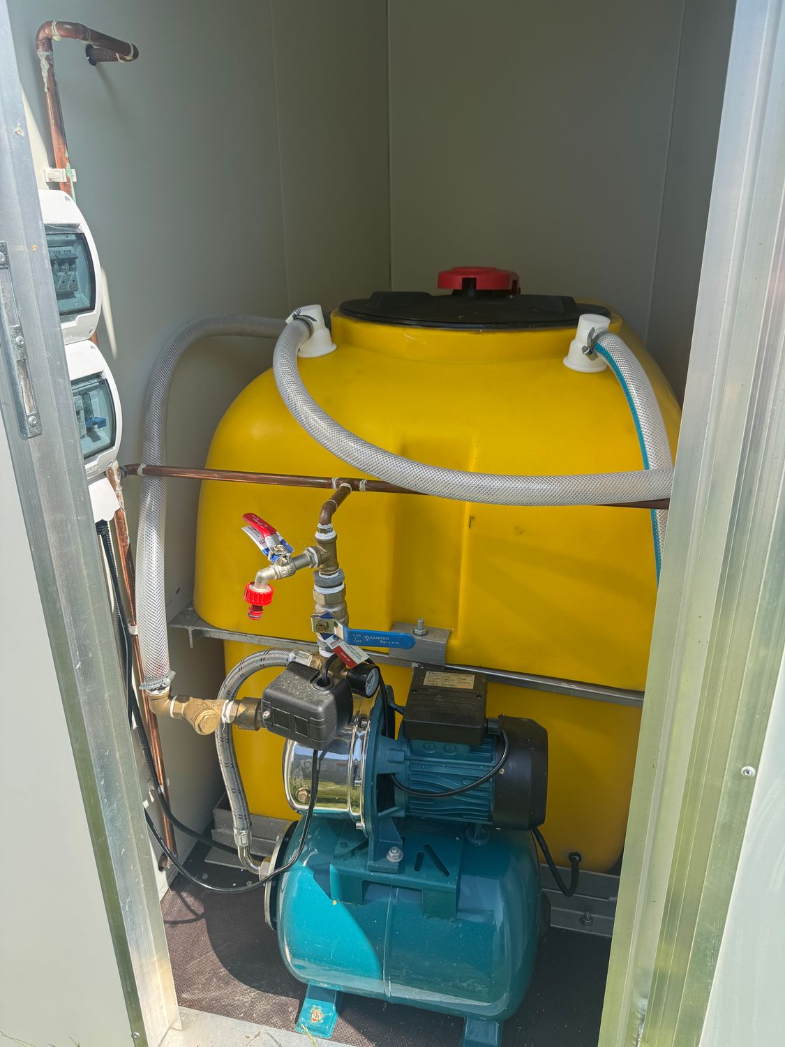 Detailaufnahme des Technikfachs mit gelbem Wassertank, Druckpumpe, Schläuchen und Sicherungskästen