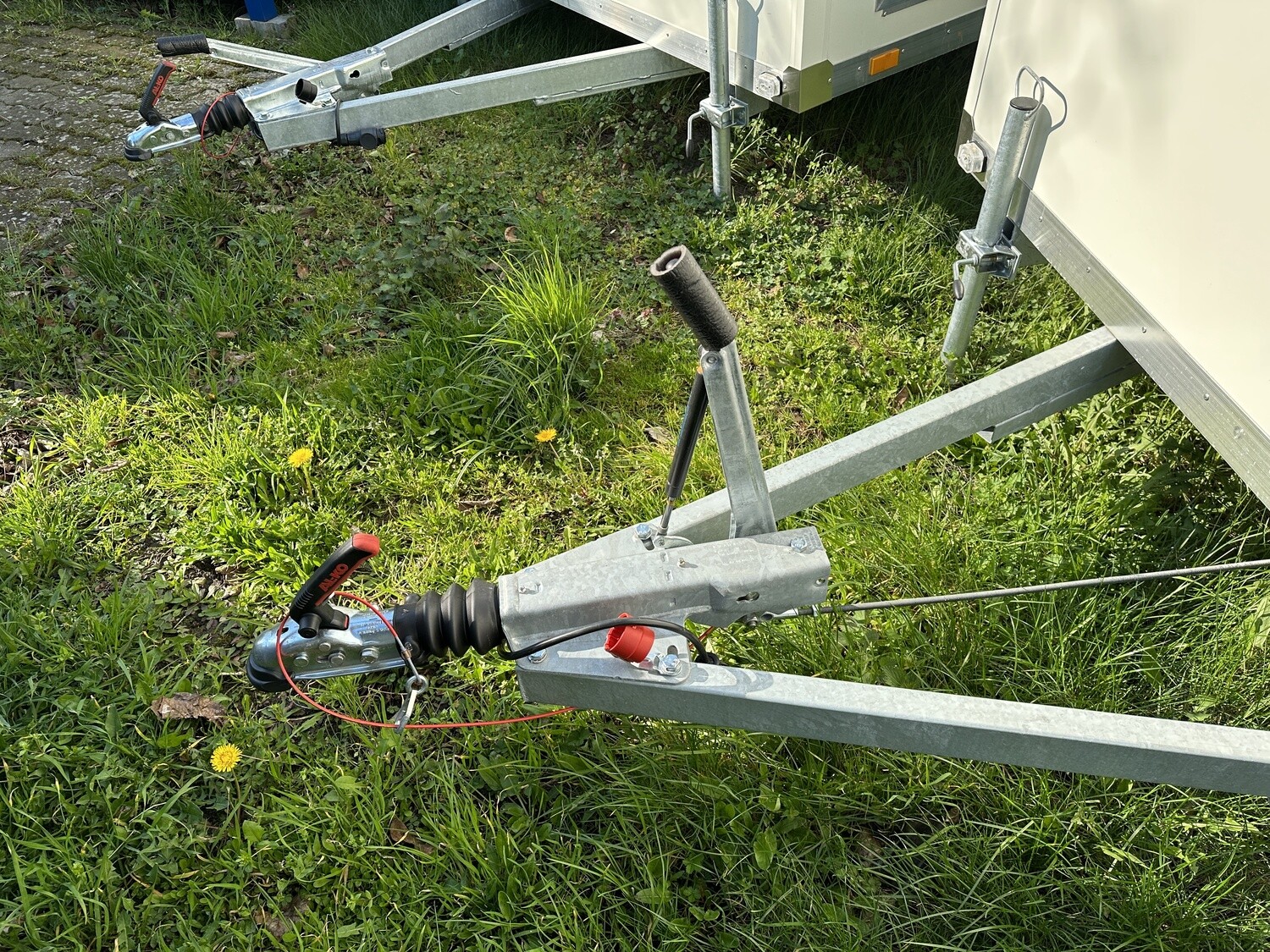 Detailaufnahme der Deichsel mit Kupplung, Abreißseil und Stützrad im Gras neben dem Anhänger