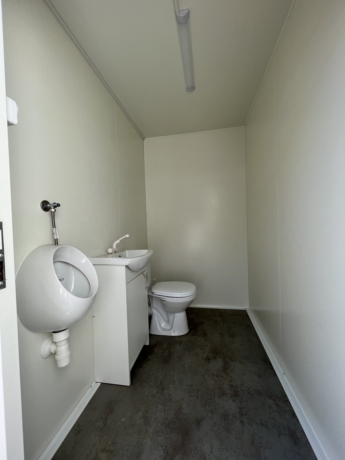Zweiter Raum des Anhängers mit Urinal, Waschbecken und WC unter einer Leuchtstoffröhre