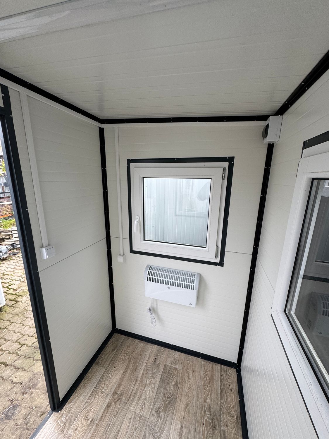 Innenansicht mit hellen Wandpaneelen, Fenster, wandhängendem Heizgerät und Boden in Holzoptik