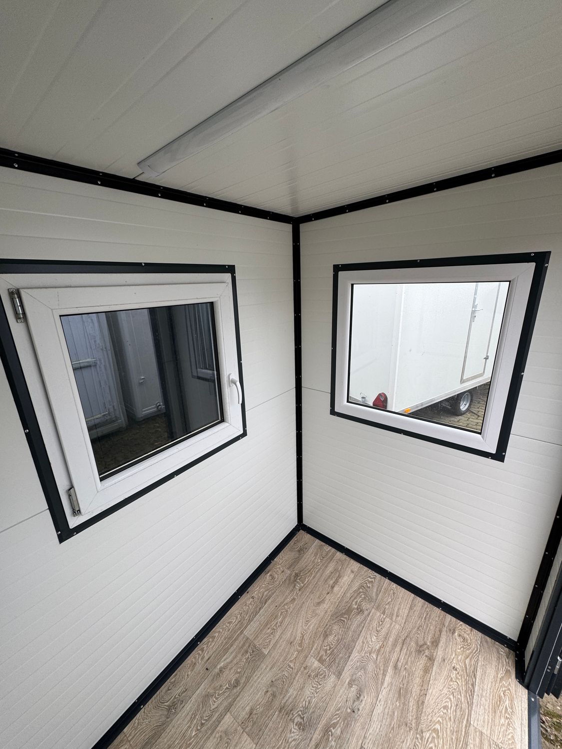 Blick in die Innenecke des 2,00 x 1,50 m großen Büros: zwei Fenster, Deckenleuchte, Holzoptikboden