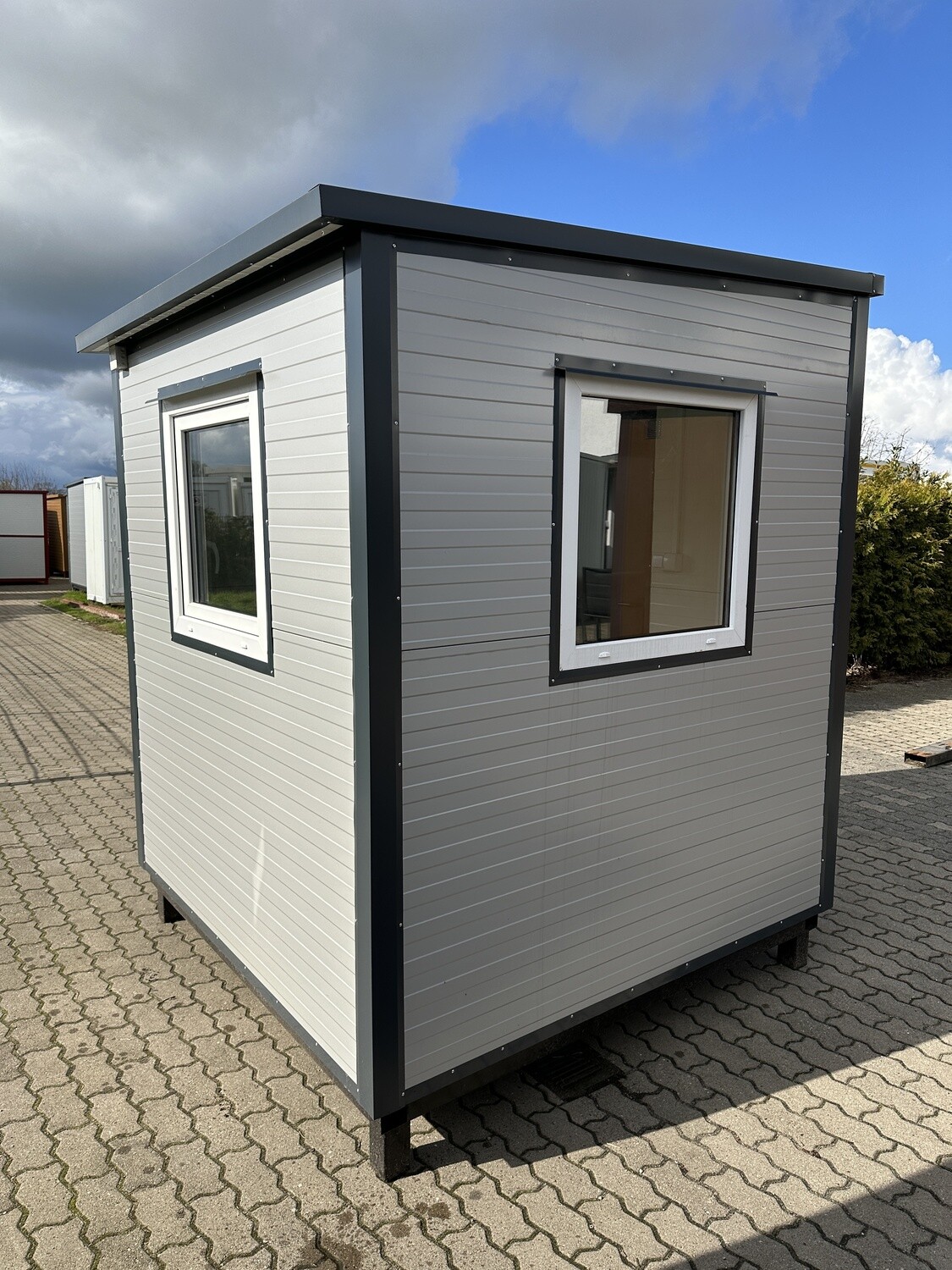 Eckansicht des kleinen Bürocontainers mit zwei weiß gerahmten Fenstern und dunkler Dachkante