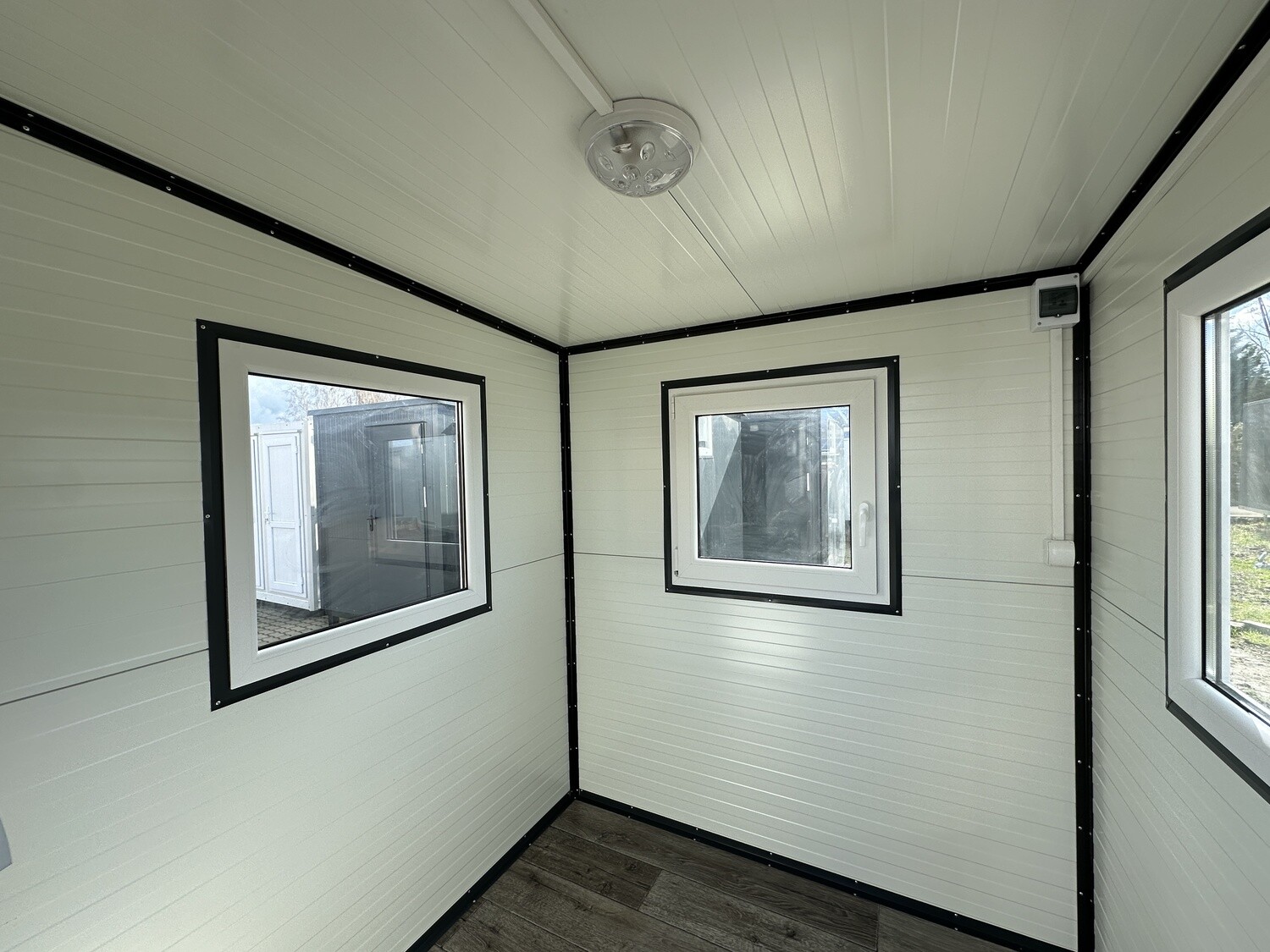 Blick in den hellen Innenraum des Bürocontainers mit mehreren Fenstern, Steckdose und Deckenleuchte