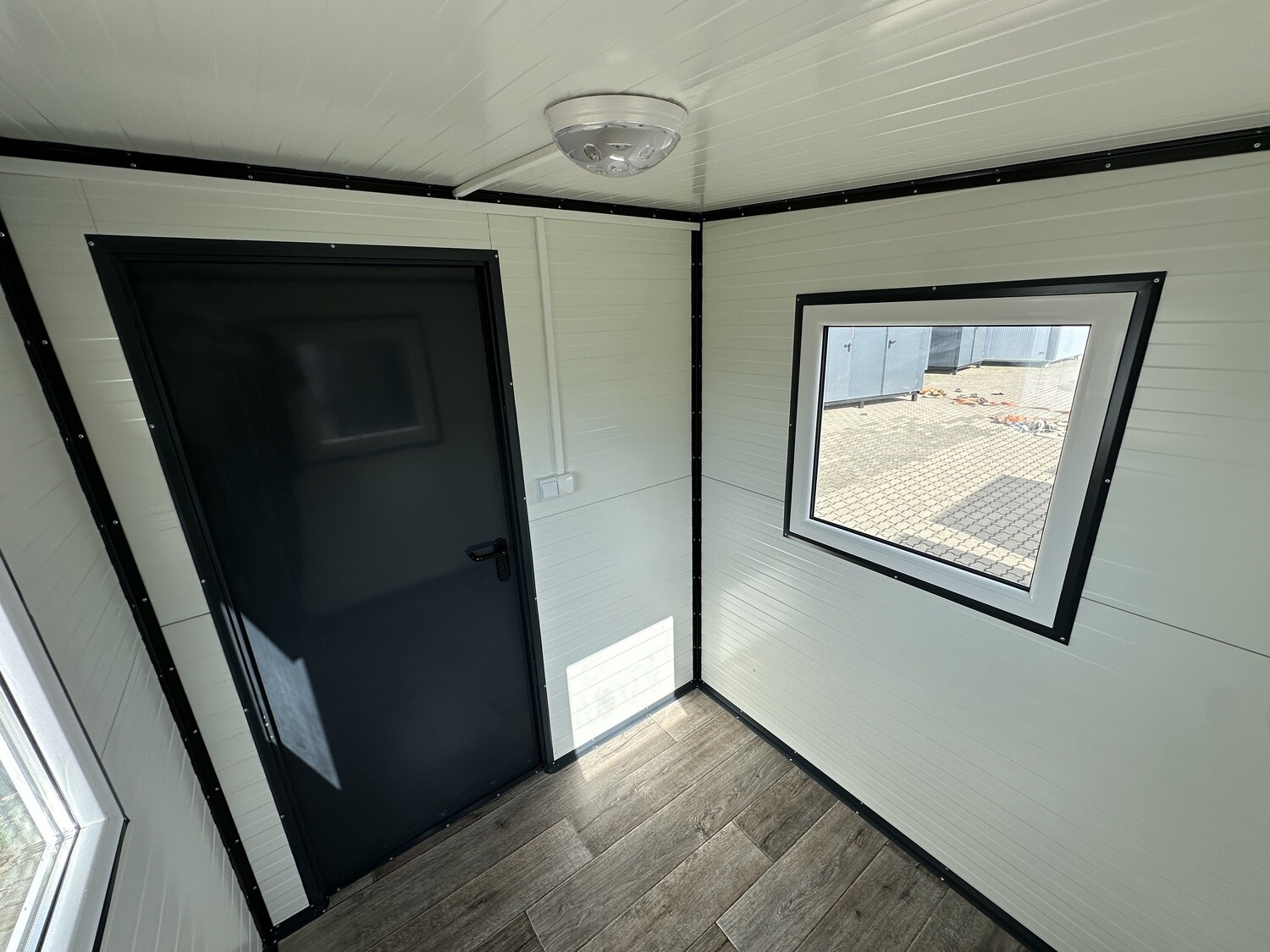 Eingangsbereich von innen: dunkle Tür, rechts ein Fenster mit Blick auf den gepflasterten Stellplatz