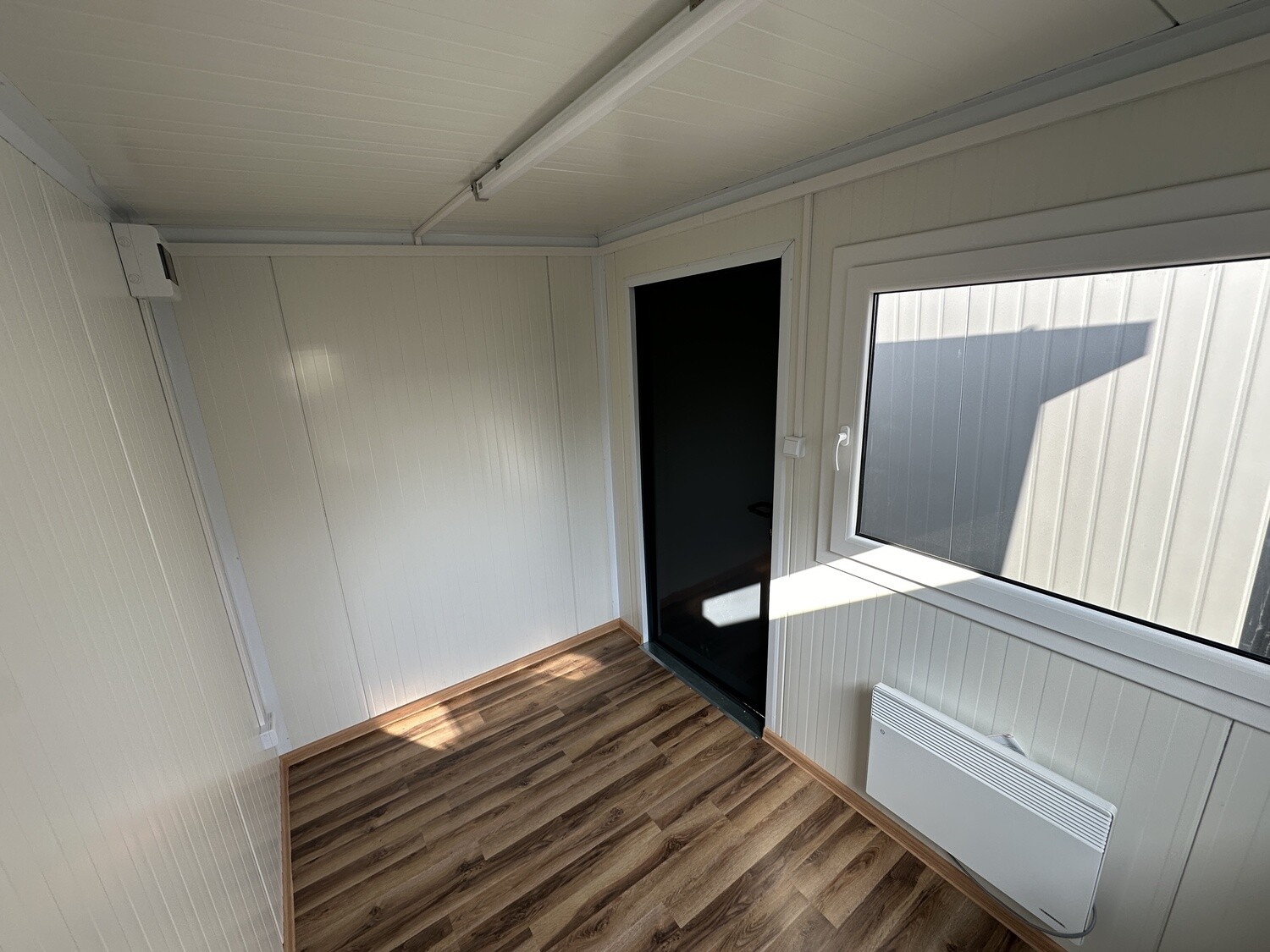 Vom Fenster aus fotografiert: Heizgerät unter der Scheibe, Deckenleuchte und helle Wandpaneele