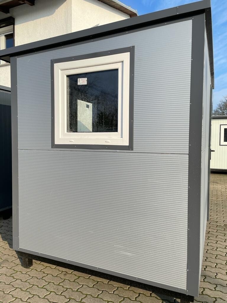 Fensterseite in Hellgrau mit dunkel abgesetztem Rahmen, aufgestellt auf einer Pflasterfläche