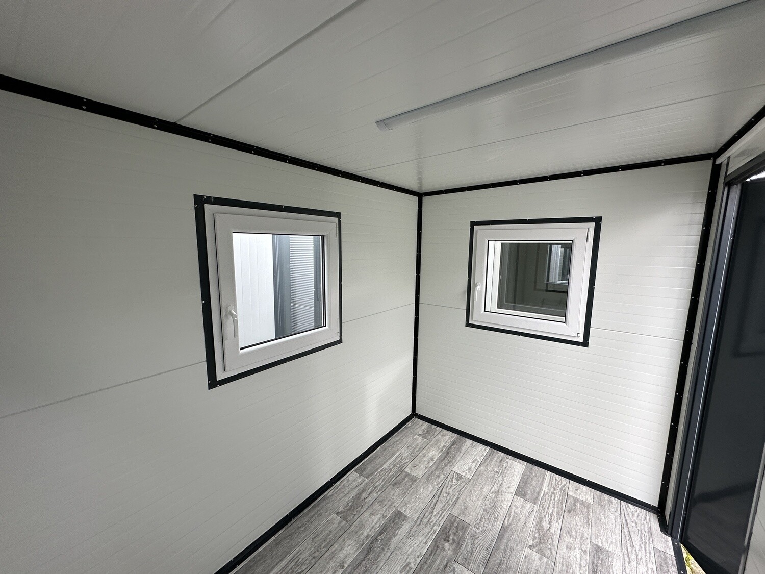 Innenecke mit zwei Fenstern, weißen Wandpaneelen und grauem Dielenboden in Holzoptik