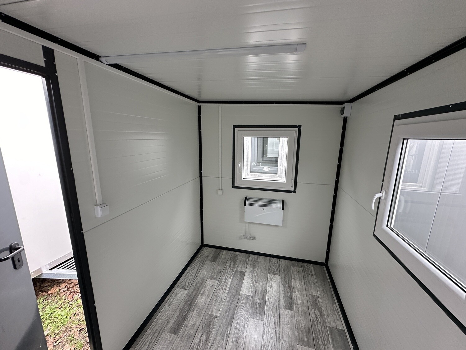 Innenaufnahme mit Heizgerät unter dem Fenster, Elektroleitung an der Wand und offener Tür links