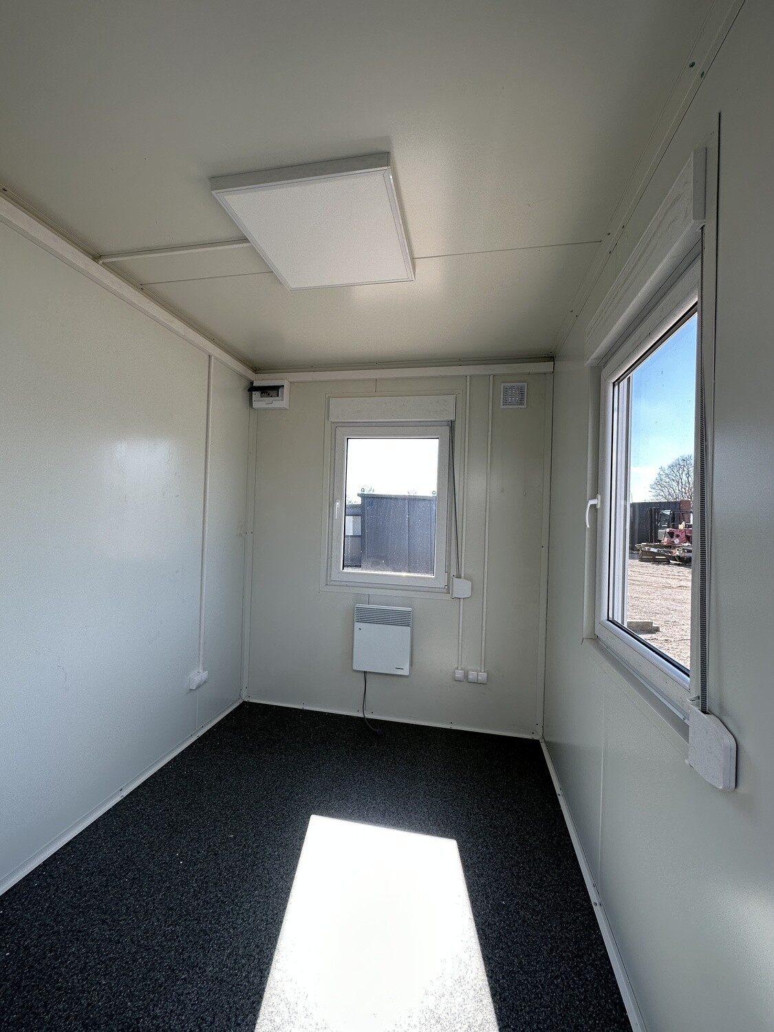 Helle Wandverkleidung, Steckdosen und dunkler Bodenbelag im leeren Bürocontainer 3,00 x 2,44