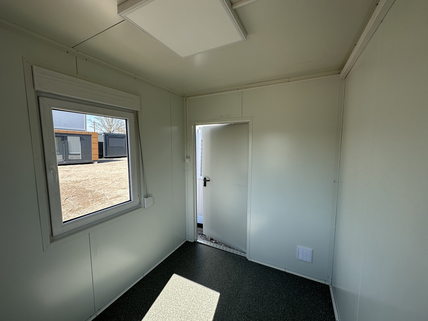 Blick zur geöffneten weißen Innentür des Bürocontainers 3,00 x 2,44, daneben ein Schiebefenster