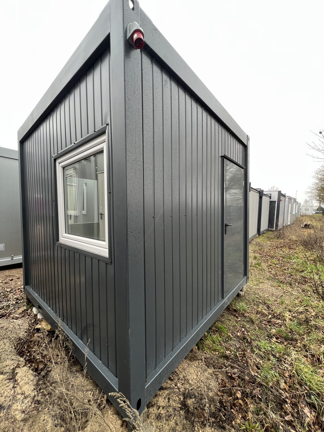 Stirnansicht mit Fenster und dunkler Außentür des Bürocontainers 3,00 x 3,00 m auf einer Wiese